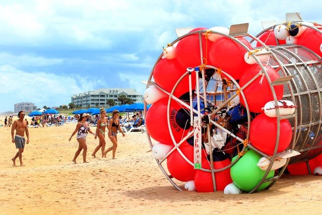 Beachgoers walk past the floating vessel that resembles a floating hamster wheel, Monday July 26, 2021 that came ashore on the beach in the Hammock north of 16th Road and Old Salt Park on Saturday with Reza Baluchi on board. Baluchi was attempting to run the vessel to New York from St. Augustine Fl..